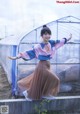 A woman standing in front of a greenhouse with her arms outstretched.