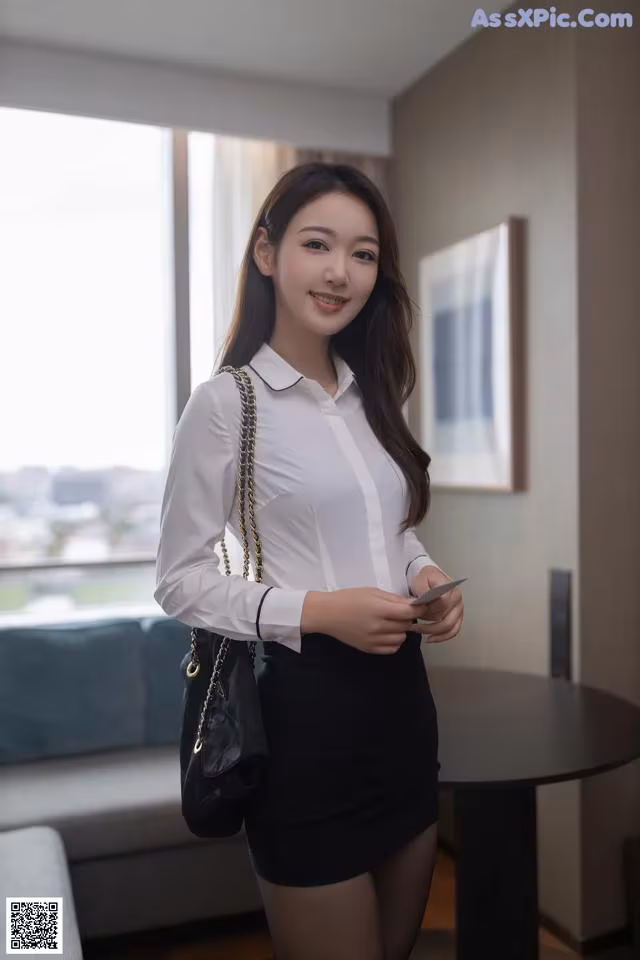 A woman in a white shirt and black skirt holding a cell phone.