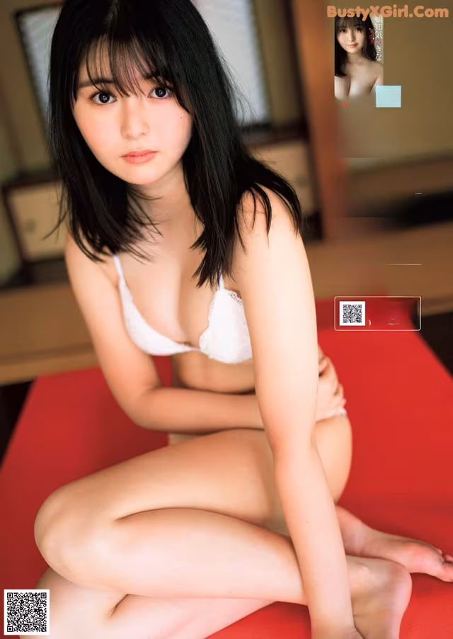 A woman in a white bra sitting on a red couch.