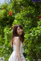 A woman in a white dress standing in front of a bush.