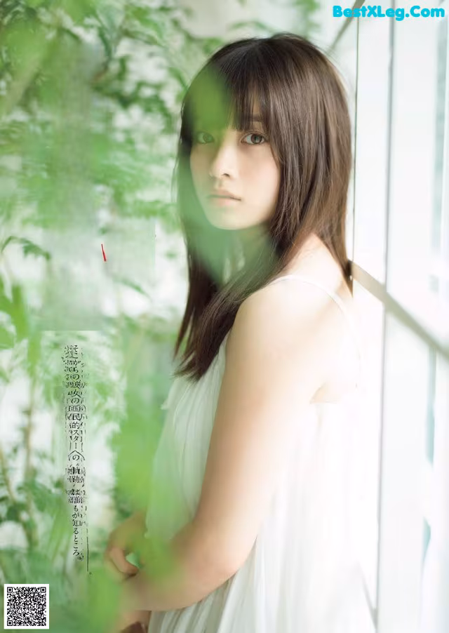A woman in a white dress standing by a window.