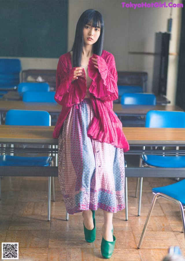 A woman standing in front of a classroom full of desks.