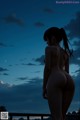 A nude woman standing on a balcony looking at the moon.