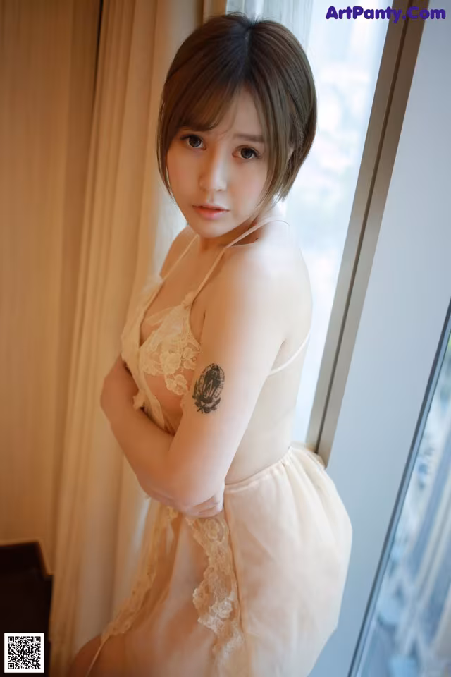 A woman with a tattoo on her arm standing by a window.
