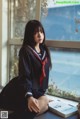 A woman in a school uniform sitting on a window sill.