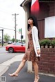 A woman in a brown dress and white cardigan is walking down the street.